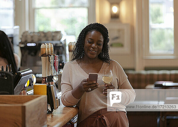 Woman with smart phone enjoying white wine in bar