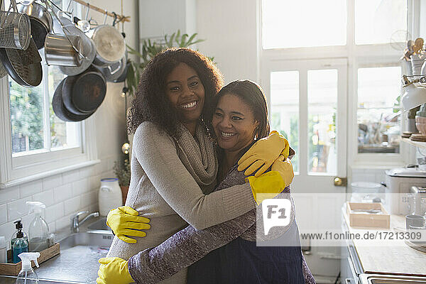 Porträt glückliche Mutter und Tochter in Gummihandschuhen umarmen in der Küche