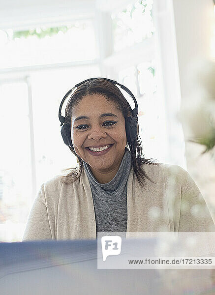 Lächelnde Frau mit Kopfhörer arbeiten von zu Hause aus am Laptop