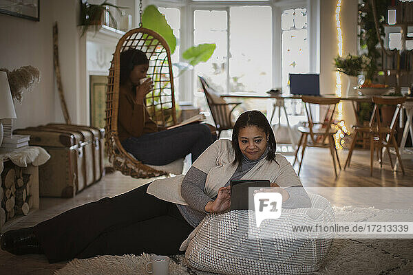 Mutter und Tochter lesen Buch und digitale Tablette im Wohnzimmer