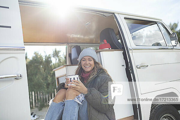 Portrait carefree young woman with coffee in sunny camper van