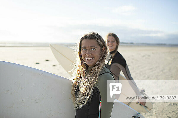 Portrait happy young female surfer with surfboard on sunny beach