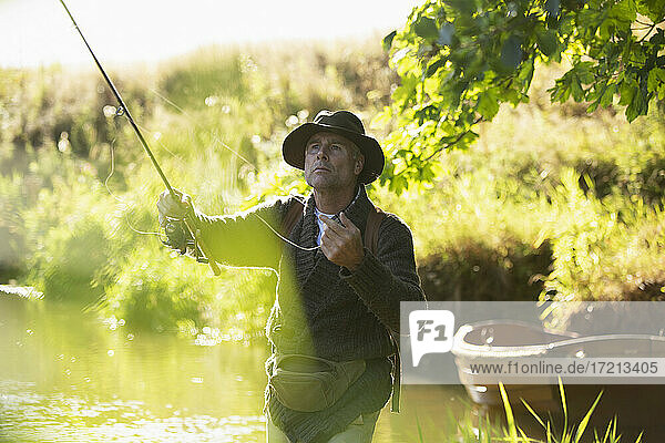 Fokussierter Mann wirft Fliegenfischerrute in sonnigen Fluss