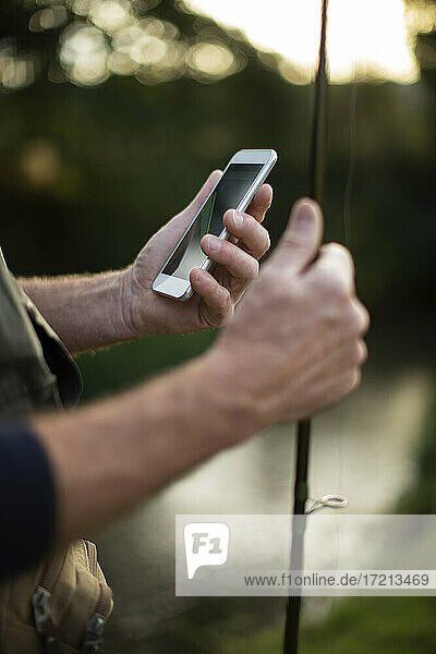 Close up man holding fishing pole and smart phone
