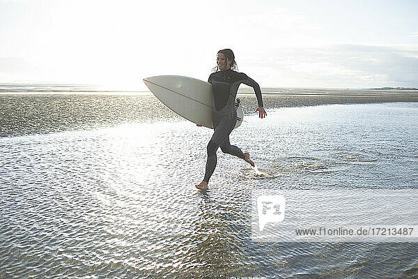 Junge weibliche Surferin läuft mit Surfbrett in sonnigen Ozean Strand Brandung