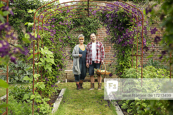 Porträt glückliches Paar ernten Gemüse unter Blume Spalier