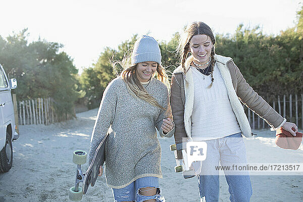Happy young women friends with skateboards on sunny beach path