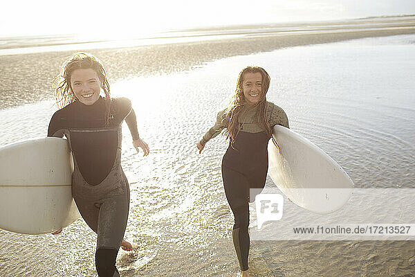 Porträt glücklich junge Surferinnen laufen mit Surfbrettern in der Brandung