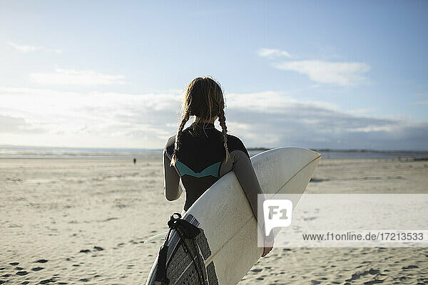 Young female surfer with braids and surfboard on sunny summer beach