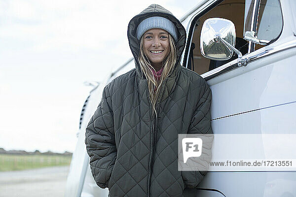 Porträt glückliche junge Frau in Kapuzenmantel vor Van