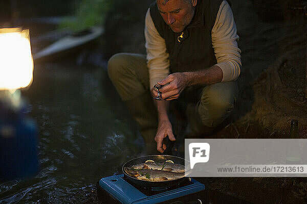 Mann kocht nachts frisch gefangenen Fisch auf Campingkocher