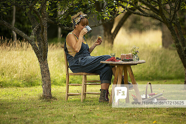 Frau macht Pause von der Gartenarbeit und isst Kuchen am Gartentisch