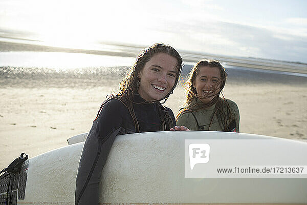 Porträt glücklich junge Surferinnen mit Surfbrett auf sonnigen Strand