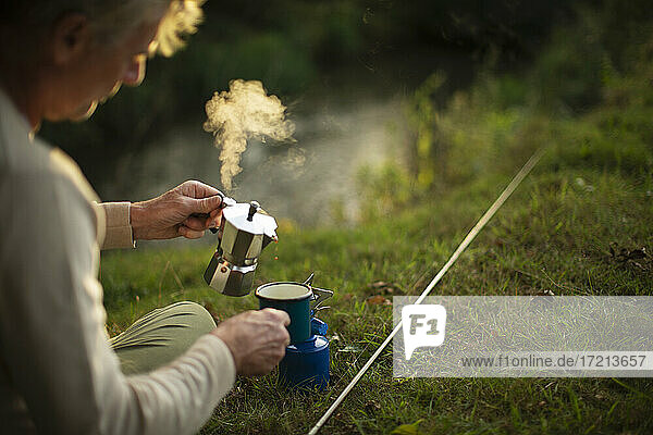 Mann macht eine Pause vom Angeln und kocht heißen Kaffee am Flussufer