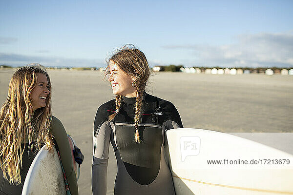 Glückliche junge Surferinnen tragen Surfbretter am sonnigen Strand
