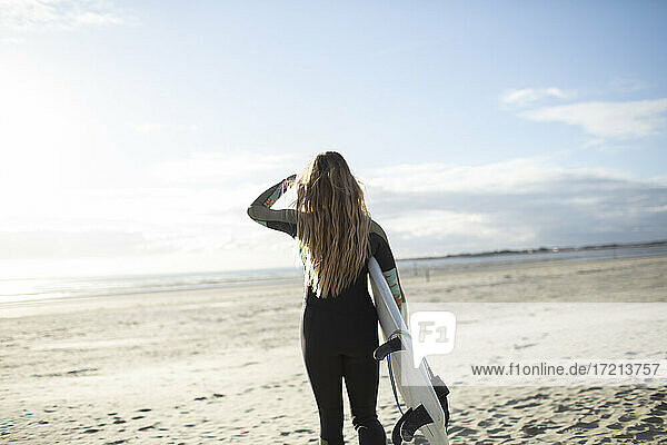 Young female surfer with surfboard on sunny tranquil summer beach