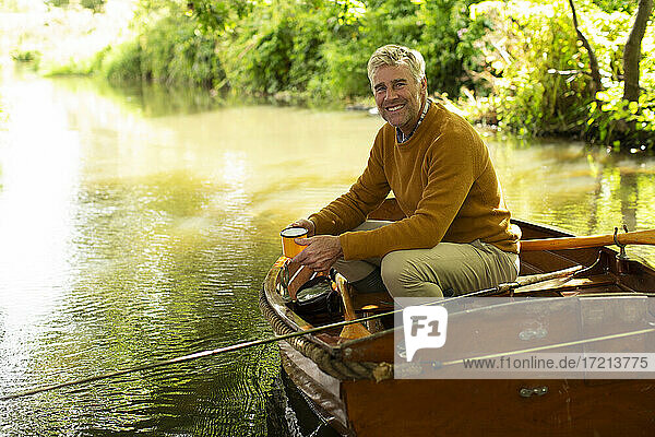 Porträt glücklicher Mann mit Kaffee Fliegenfischen in Boot auf Fluss