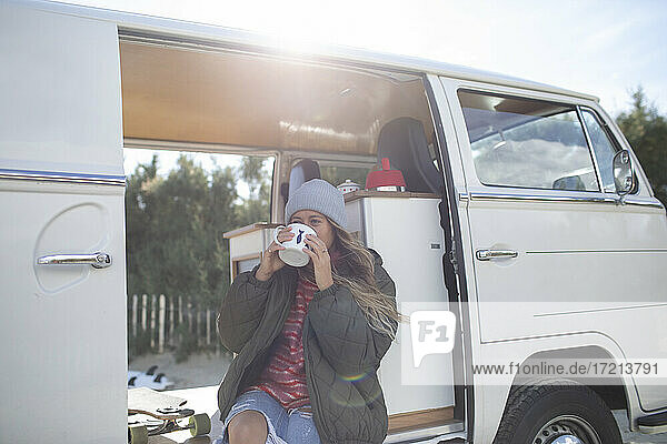 Junge Frau trinkt Kaffee in der sonnigen Tür eines Wohnmobils