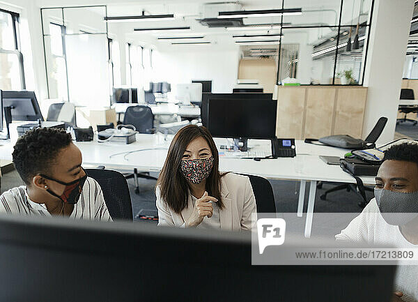 Business people in face masks working at computer in open plan office