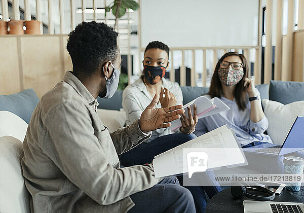 Business people in face masks discussing paperwork on office sofa