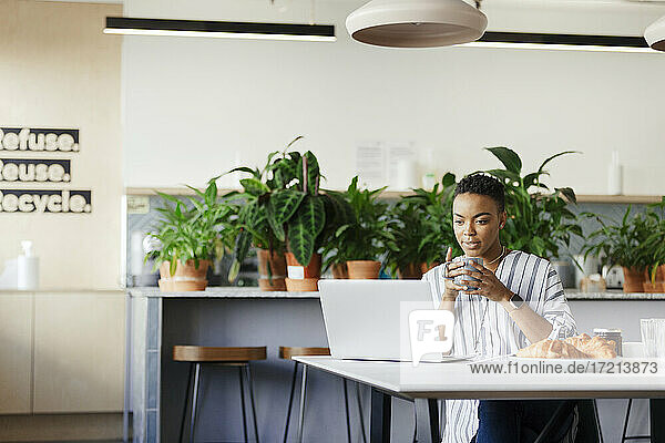 Businesswoman with coffee working at laptop in morning office lounge