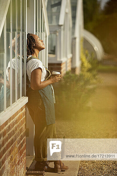 Gelassene Gartenladenbesitzerin sonnt sich mit Kaffee im Sonnenlicht