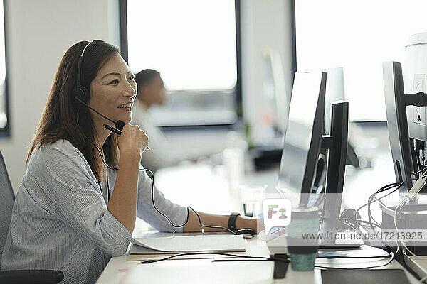 Lächelnde Geschäftsfrau mit Headset arbeitet am Computer im Büro