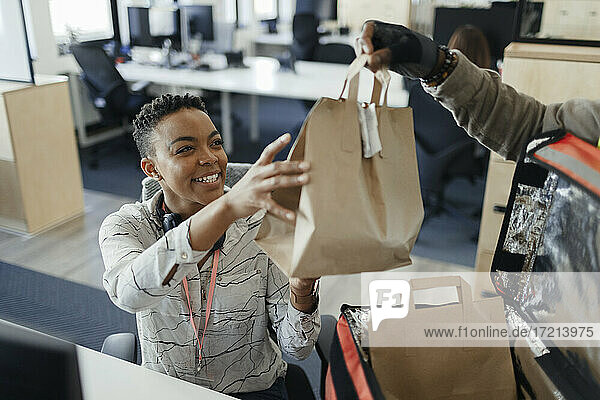 Glückliche Geschäftsfrau empfängt Mittagessen Tasche von Kurier im Büro