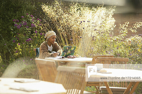 Frau arbeitet am Laptop auf der Terrasse eines sonnigen Gartencafés