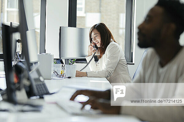 Geschäftsfrau spricht am Telefon bei sonnigen Bürofenster