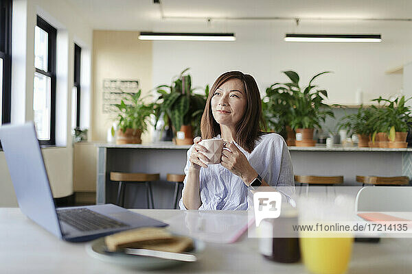 Happy businesswoman drinking coffee at laptop in office lounge