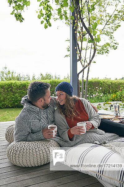 Zärtliches Paar entspannt mit Kaffee auf Kissen auf der Terrasse