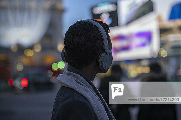 Young woman in headphones on city street at night