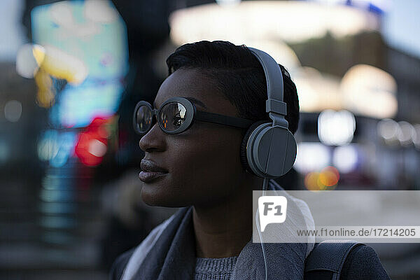 Selbstbewusste stilvolle junge Frau mit Kopfhörer auf städtischen Straße