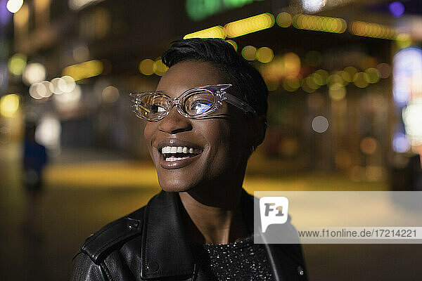 Happy young woman in funky glasses on city street at night
