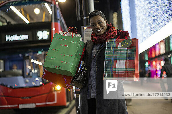 Porträt glückliche junge Frau mit Weihnachtsgeschenken in der Stadt bei Nacht