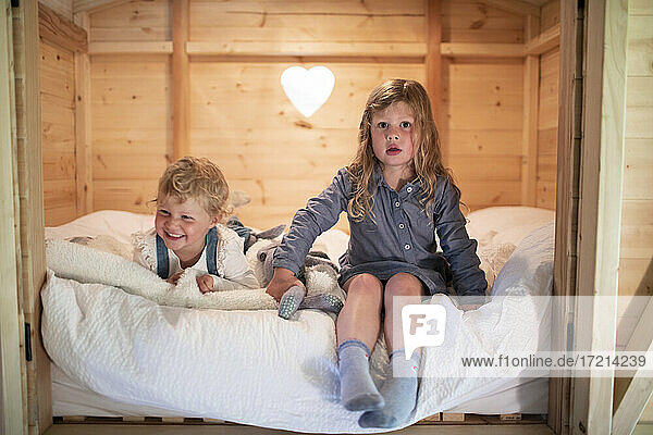 Portrait cute sisters on bed in cabin