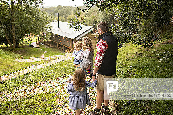 Familie  die auf einem Pfad oberhalb einer Hütte im Wald spazieren geht