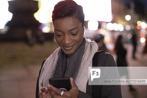 Junge Frau mit Smartphone auf dem Gehweg in der Stadt bei Nacht