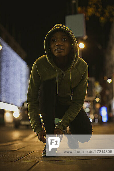 Junge Läuferin bindet Schnürsenkel auf städtischen Bürgersteig in der Nacht