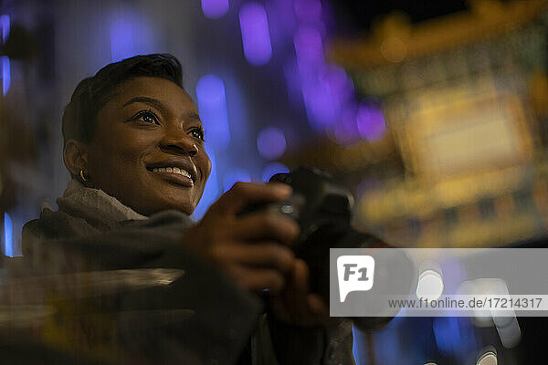Glückliche junge Frau mit Kamera in der Stadt bei Nacht