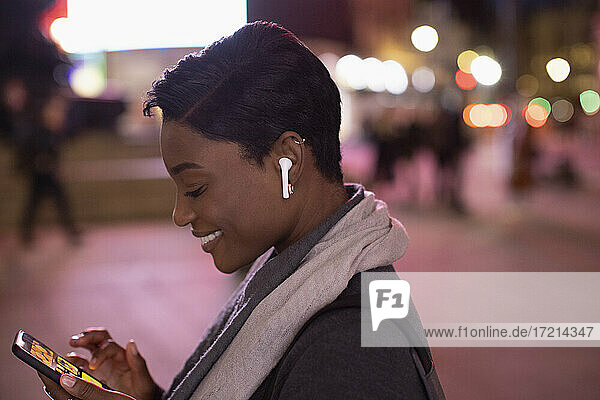 Junge Frau mit Ohrstöpsel Kopfhörer mit Smartphone in der Stadt in der Nacht