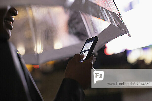 Close up junge Frau mit Smartphone unter Regenschirm in der Nacht