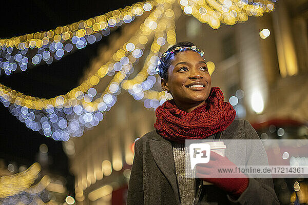 Glückliche junge Frau mit Weihnachtslicht Stirnband in der Stadt in der Nacht