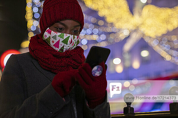 Junge Frau in Weihnachten Gesichtsmaske und Schal mit smart phone