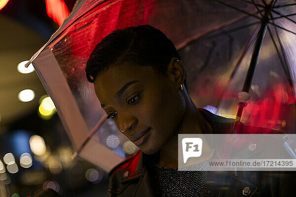 Junge Frau unter Regenschirm und Neonlichter in der Nacht