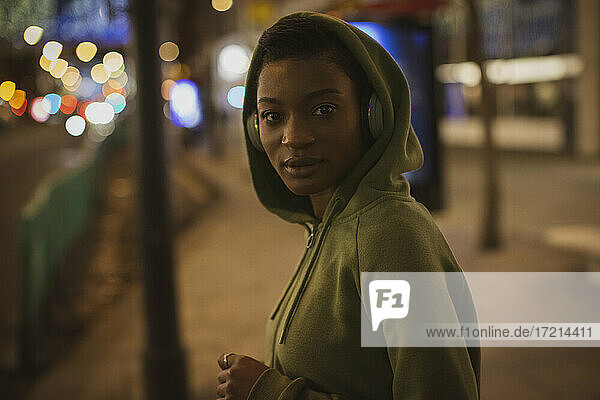 Portrait confident young woman in hoody on city sidewalk at night
