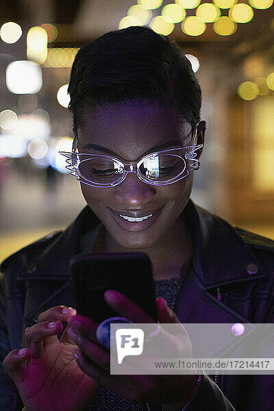 Junge Frau in funky Brille mit Smartphone in der Nacht