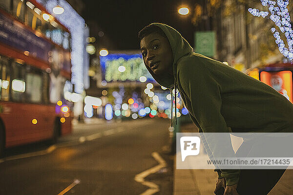 Young female jogger waiting to cross city street at night  London  UK