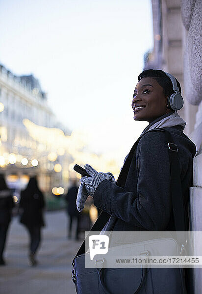 Junge Geschäftsfrau mit Kopfhörern und Smartphone auf dem Bürgersteig der Stadt